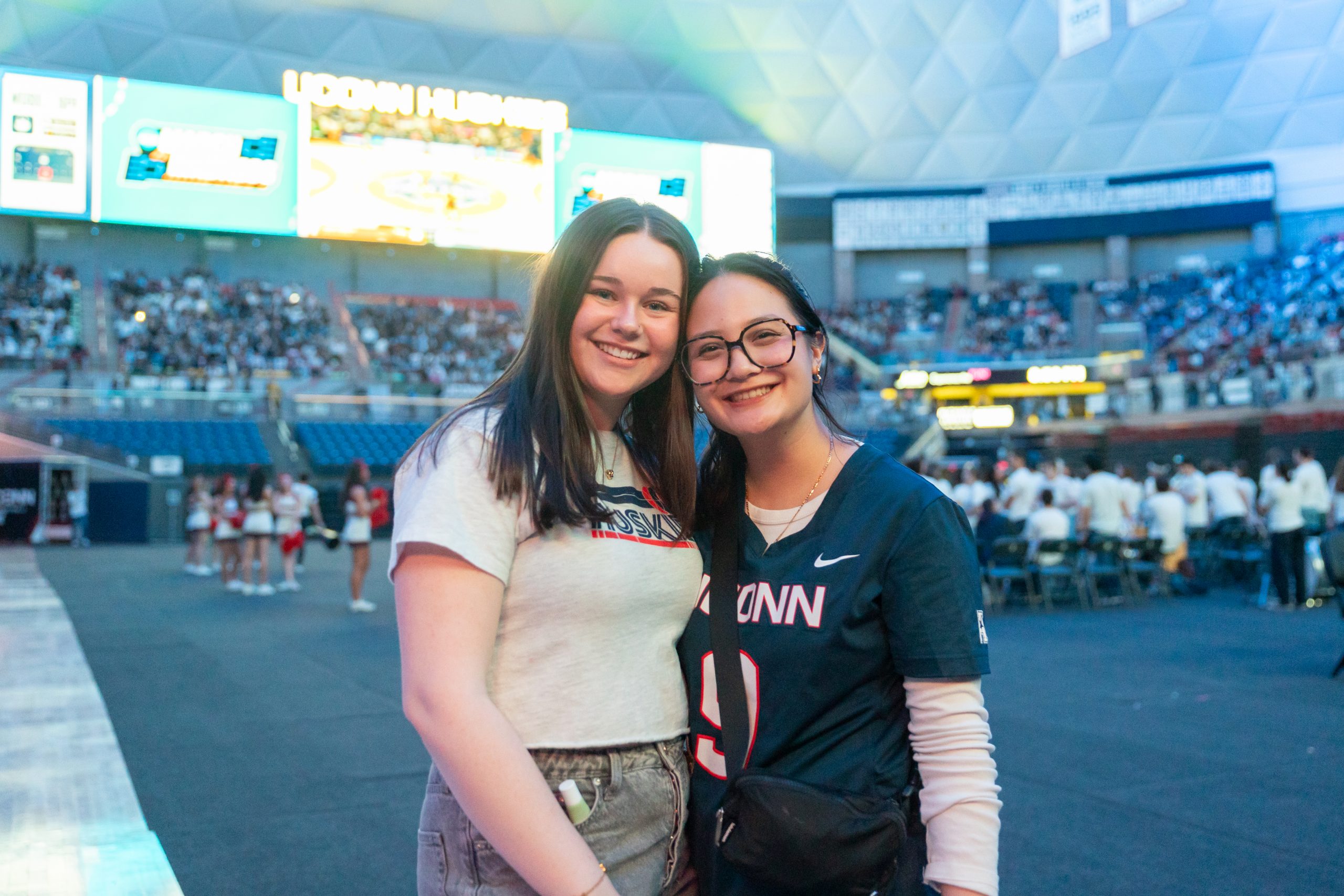 Lily Johnson '28 (CLAS), left, and Lily Cayangyang '25 (CLAS), right, pose for a photo together on the floor of Gampel Pavilion while covering the women's basketball Final Four game watch party for University Communications on Friday, April 4, 2025. (Sydney Herdle/UConn Photo)